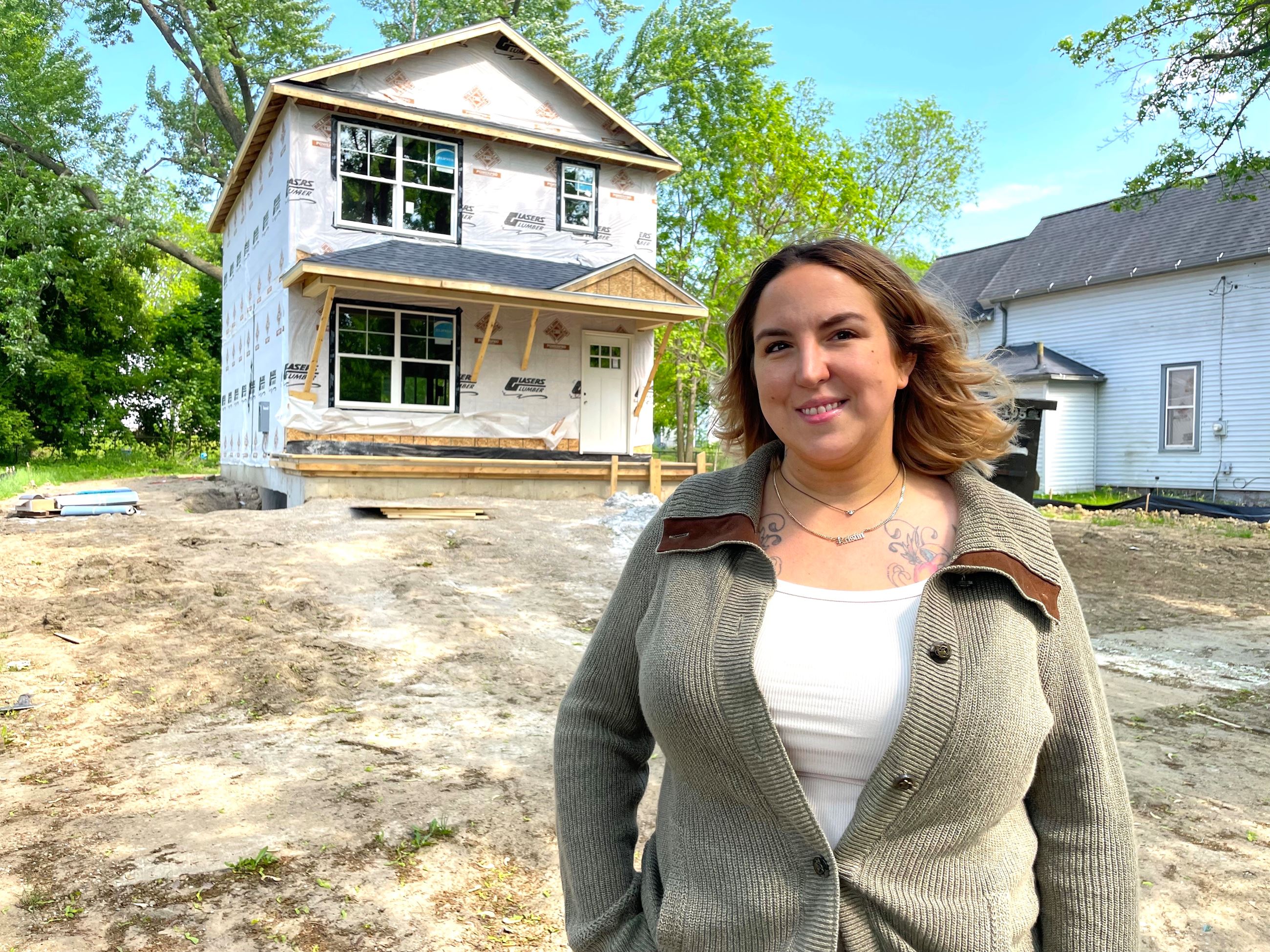 Woman smiles in front of house under construction 
