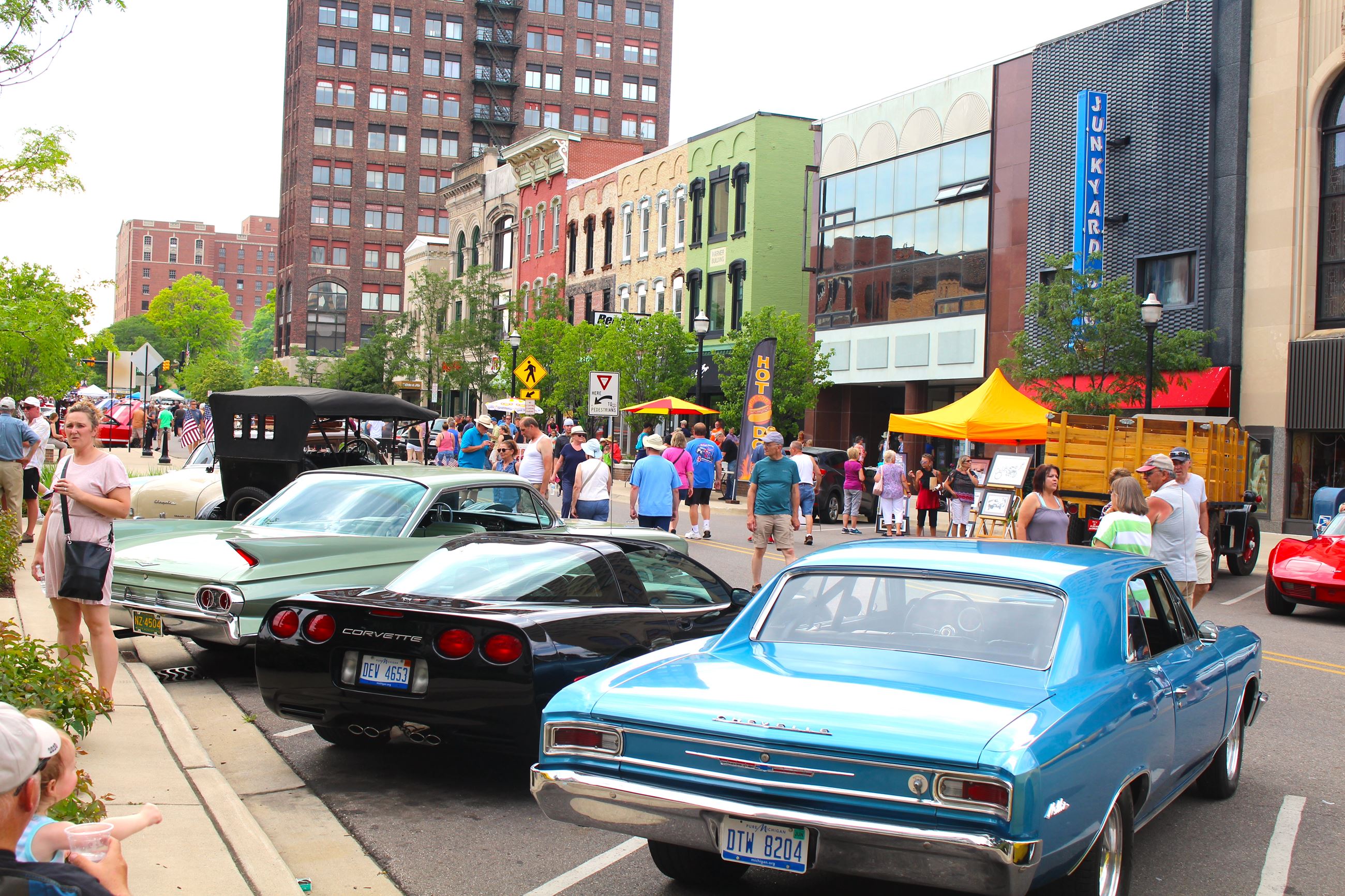 People walk by classic cars parked on a downtown street 