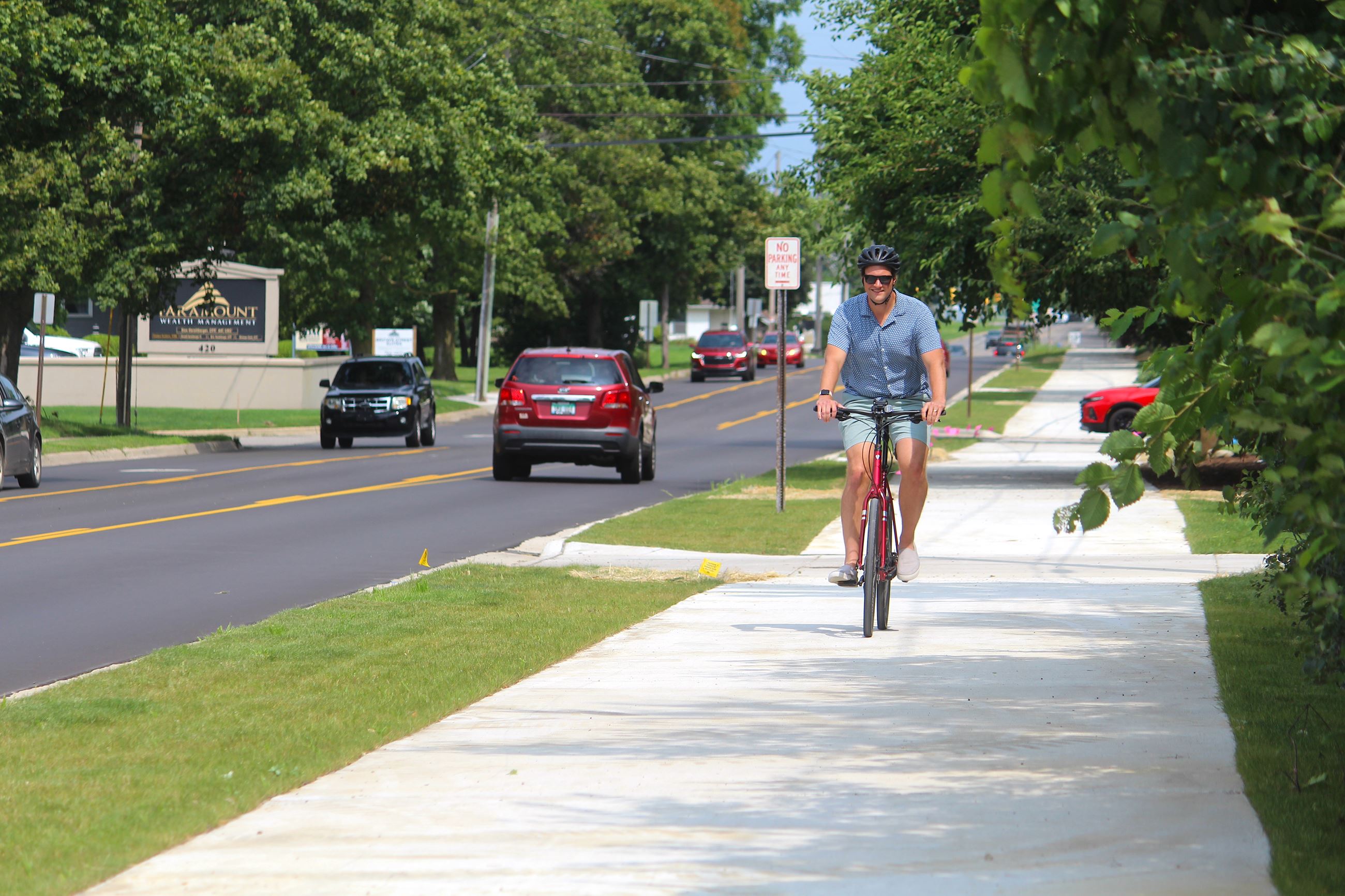Man riding a red bike on a paved pedestrian trail next to a new street surface 
