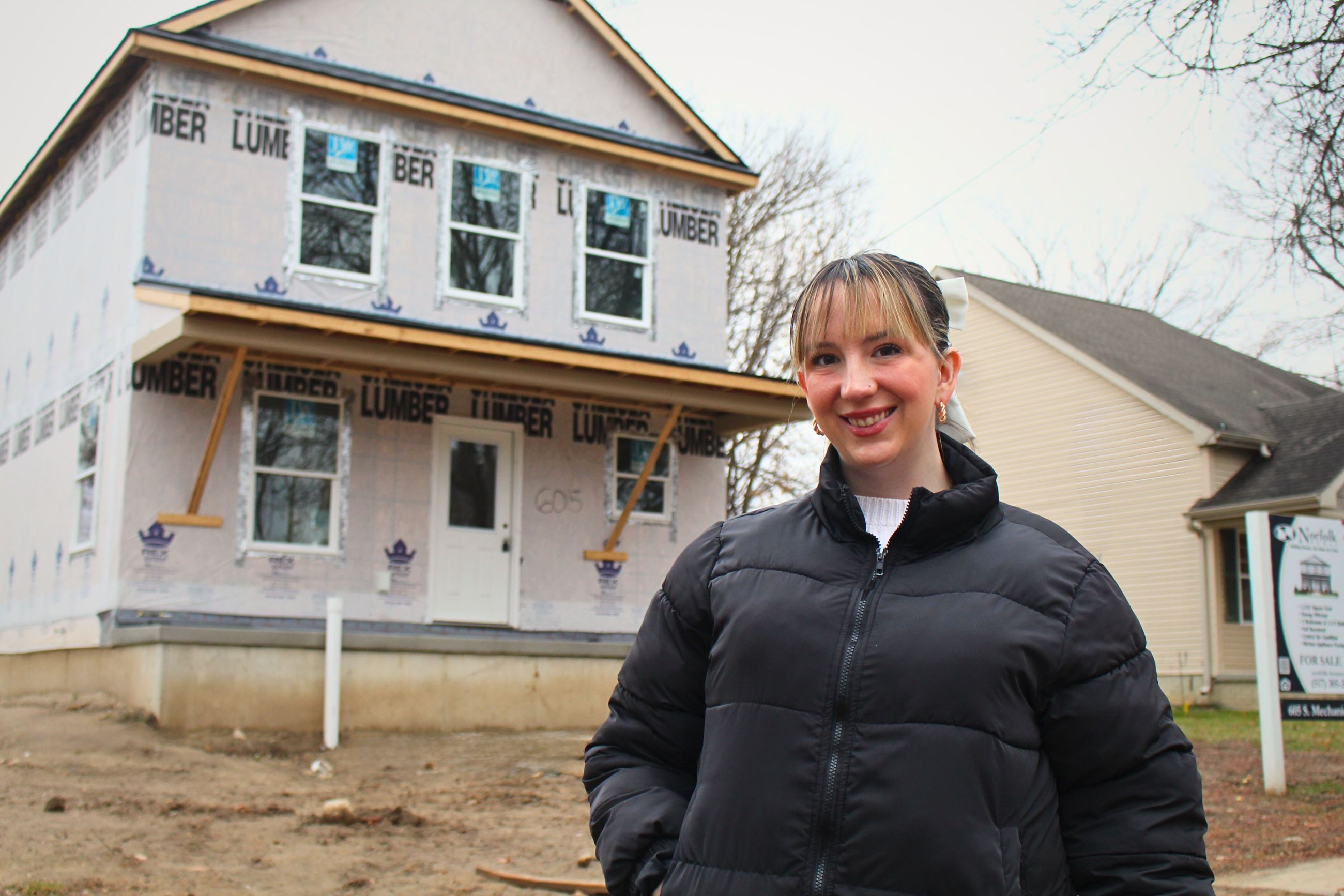 A woman stands in front of a house under construction 