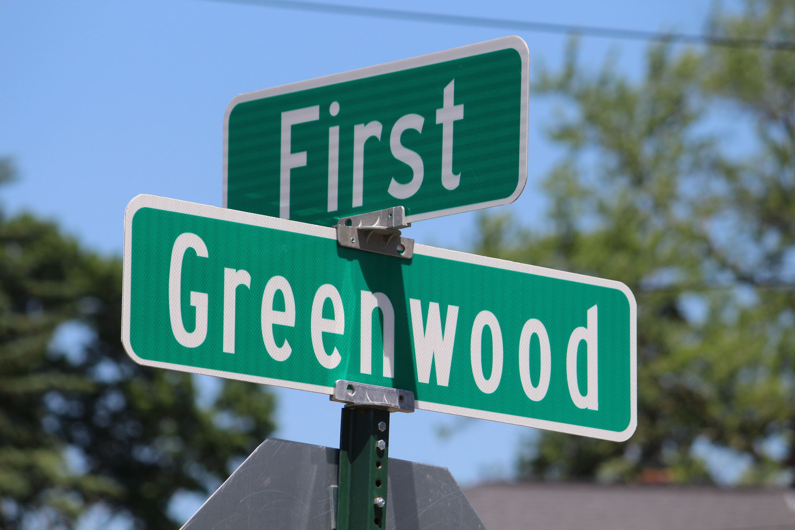 A green and white street sign that says Greenwood, First 