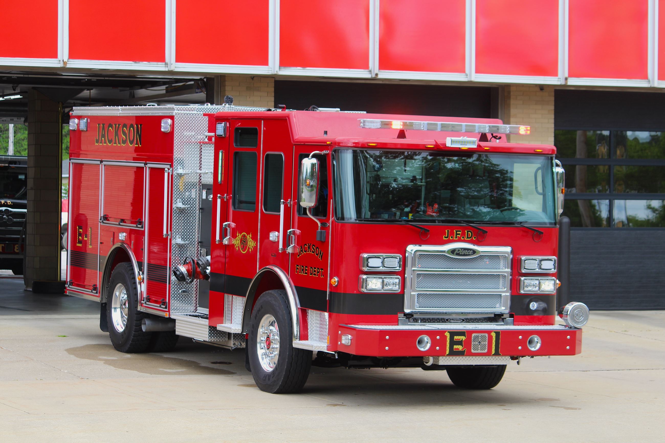 A big red shiny new fire truck is parked on concrete outside a modern fire station 