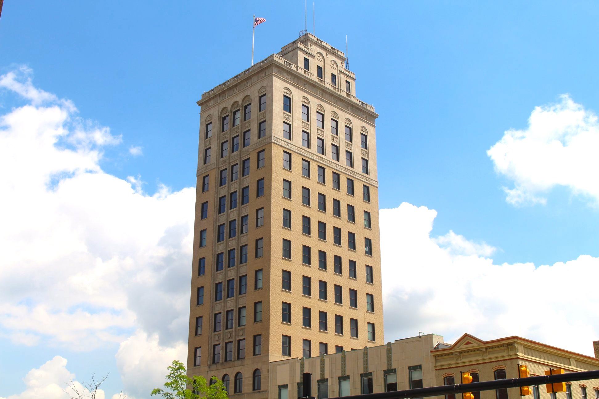 A tall cream brick skyscraper. 13 stories. Against a blue sky with fluffy clouds. 