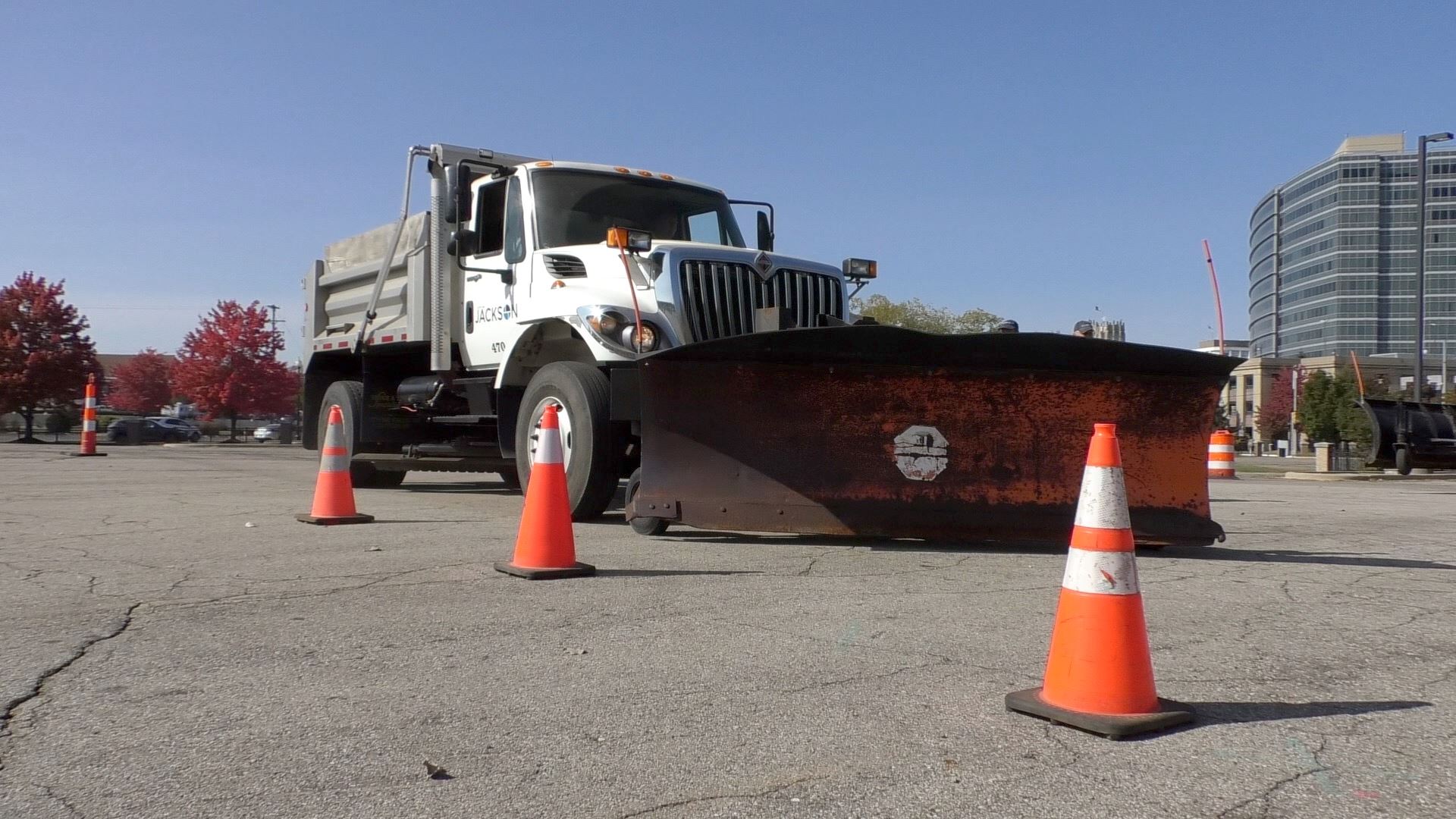 A white snow plow truck drives through orange cones on a sunny day 