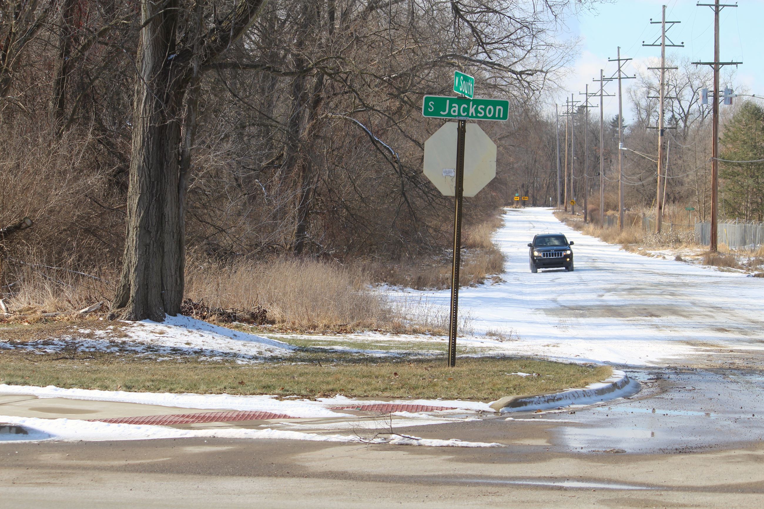 a snowy dirt road with a street sign on a sunny day. a car drives down the road. 