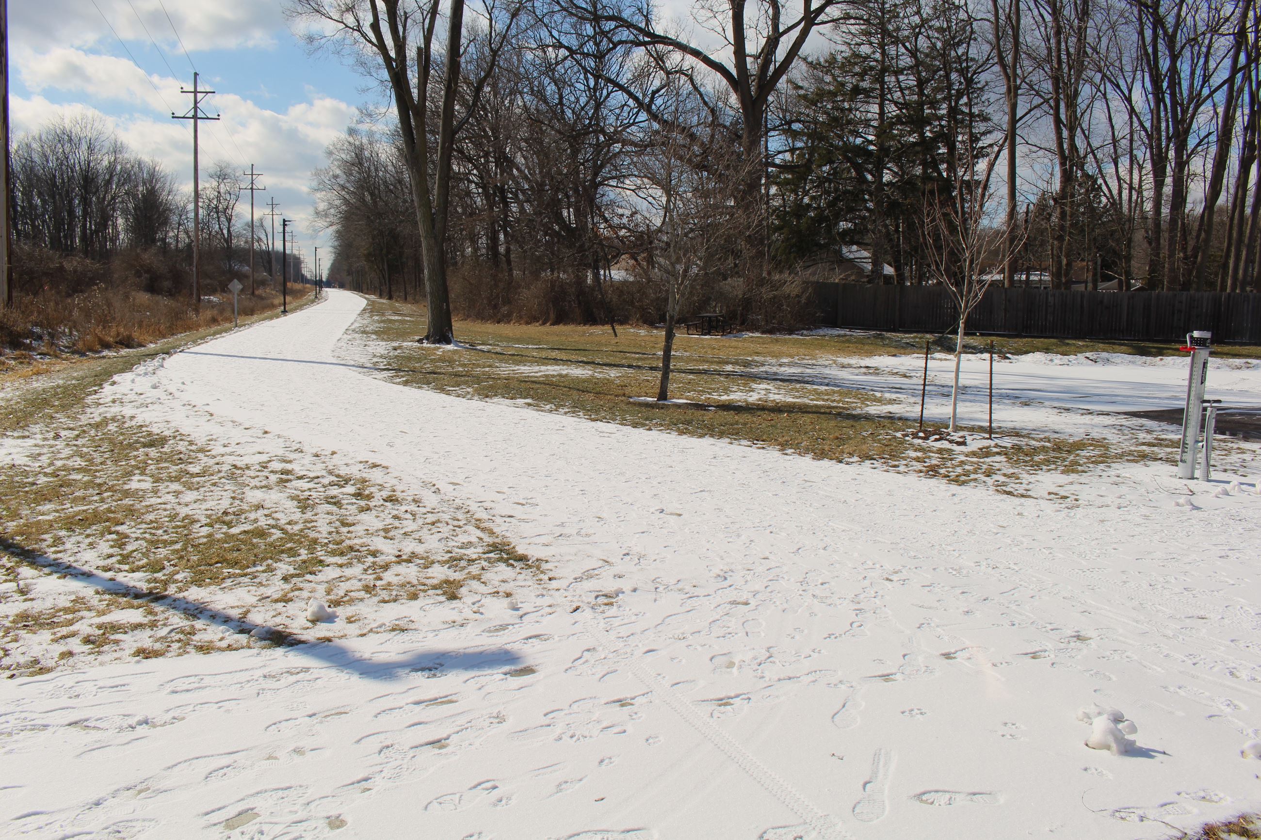A snowy pedestrian trail flanked by grass and trees