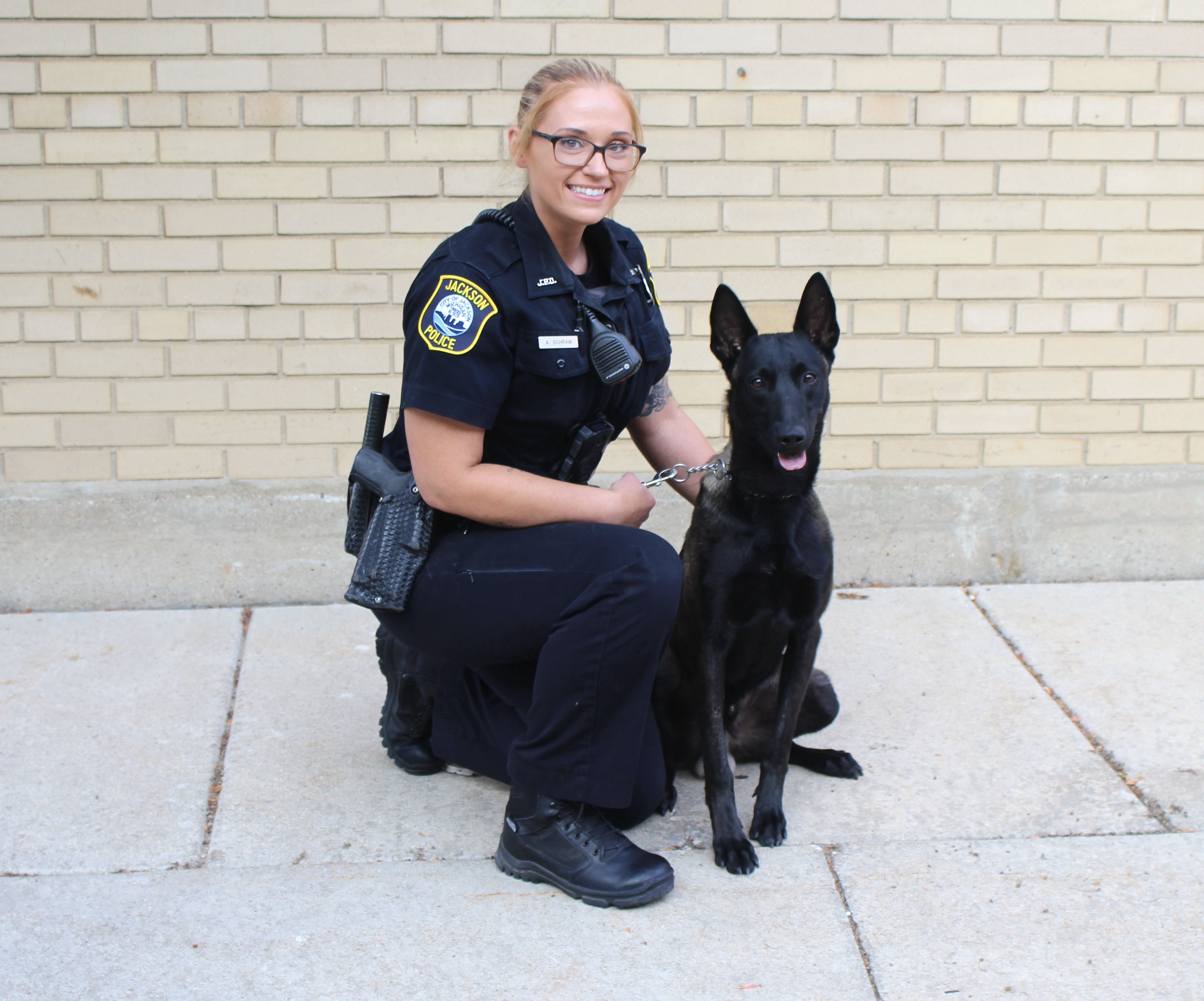 A female police officer poses with a black police dog. 