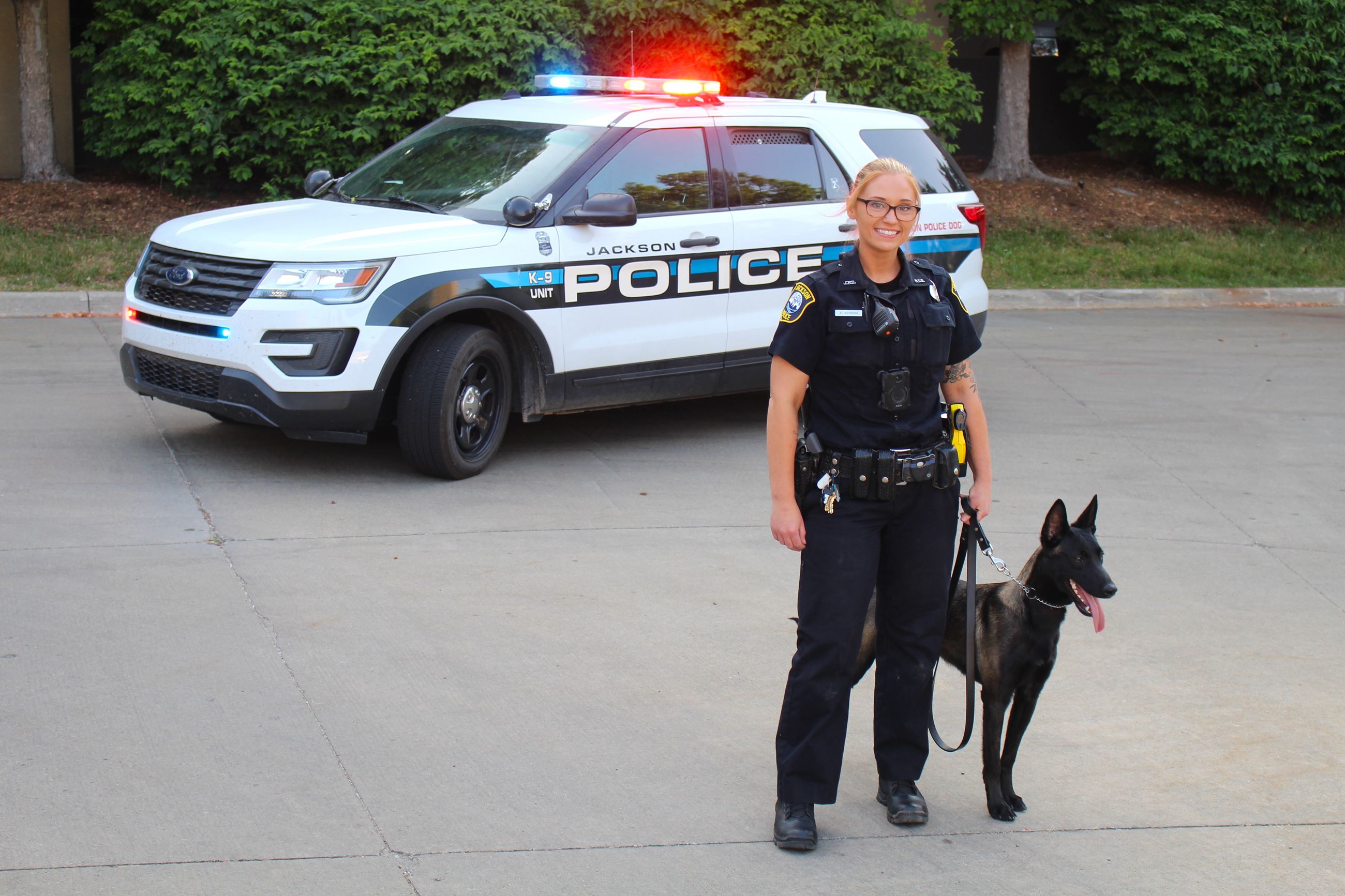 A female police officer poses with a black police dog.